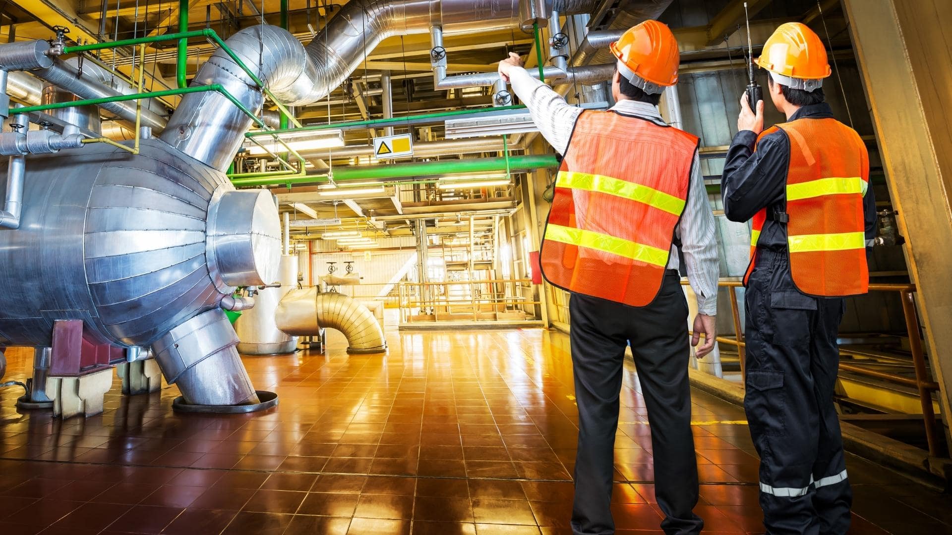 Two men wearing hard hat talking at a factory.