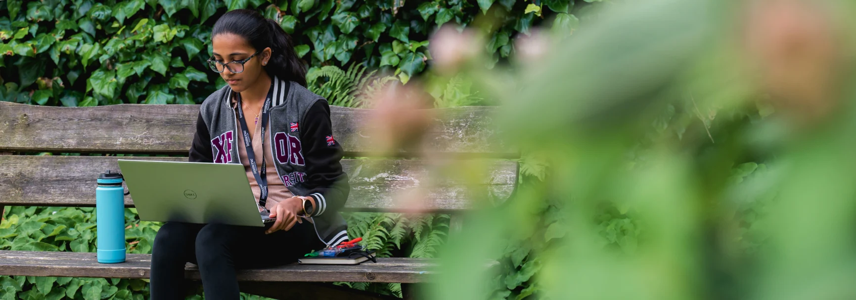 A woman with a laptop sitting on a bench outside