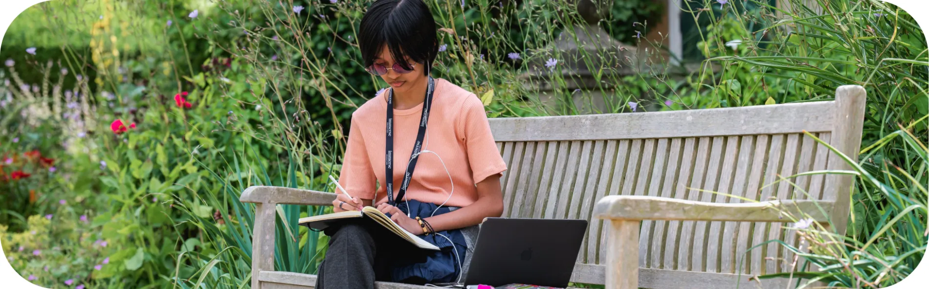 A student sitting on the bench outside writing on her notebook.