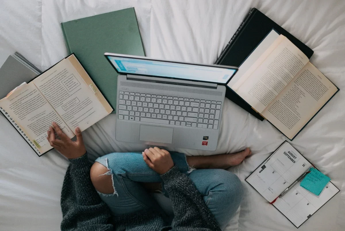 Creative writing student surrounded by notepads using laptop to respond to a prompt