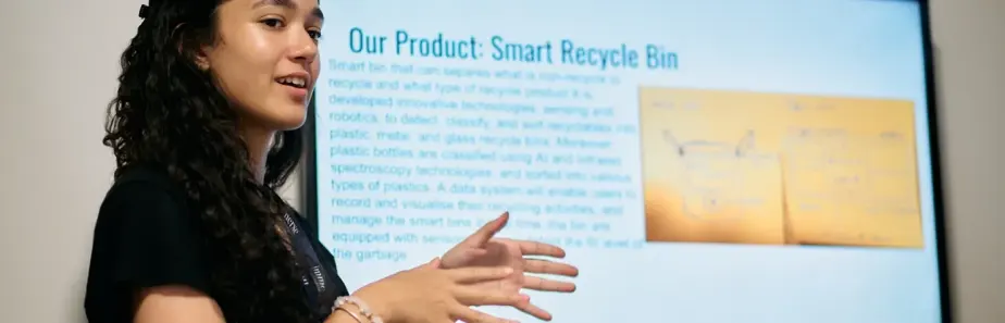 A student engaged in a business management program with Immerse Education, presenting on a product they've designed called 'smart recycle bin'.