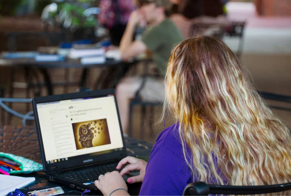 A student focused on studying with a laptop and books, part of their EPQ project preparation.