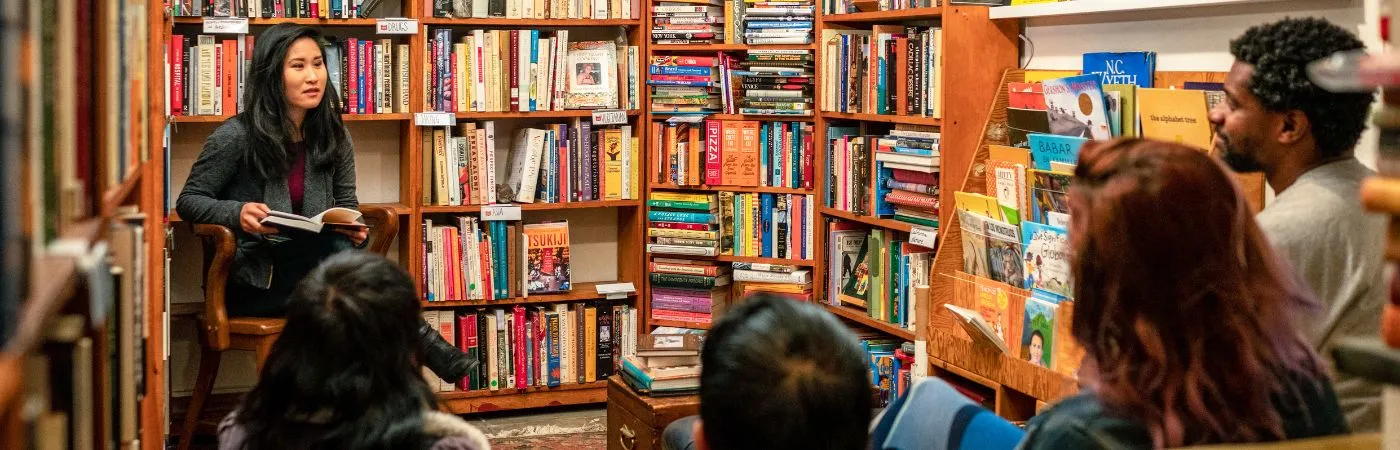 An author at a library, working on publishing a book, with shelves of books in the background.