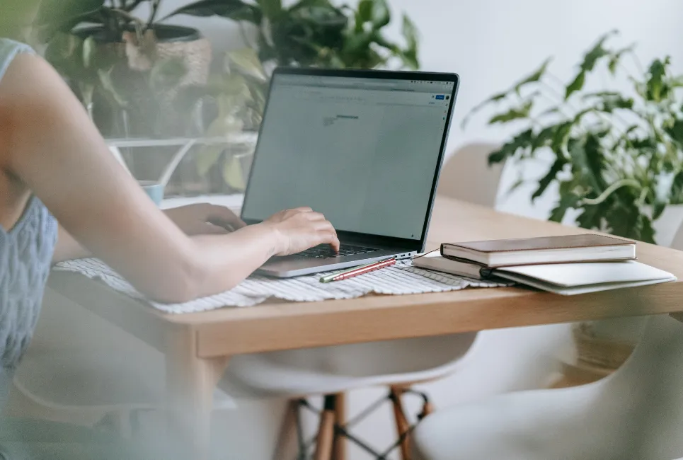 Close-up of hands typing on a laptop keyboard with a notebook and coffee cup on the desk.