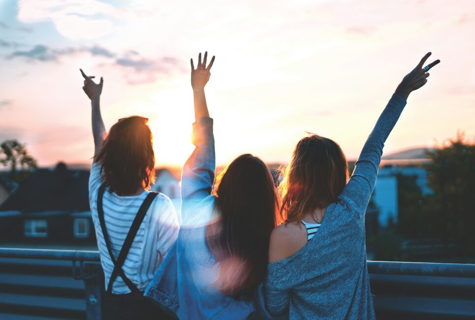 Back of three friends raising hands up in air