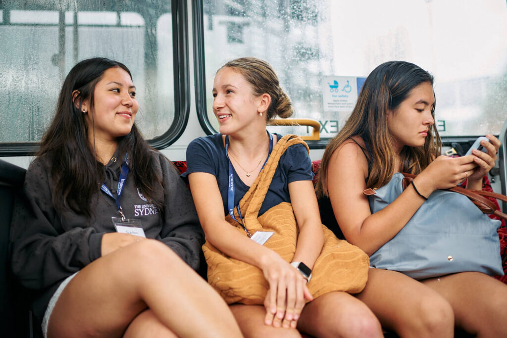 3 teen students chatting during an excursion on a bus during academic summer camp in Sydney, Australia