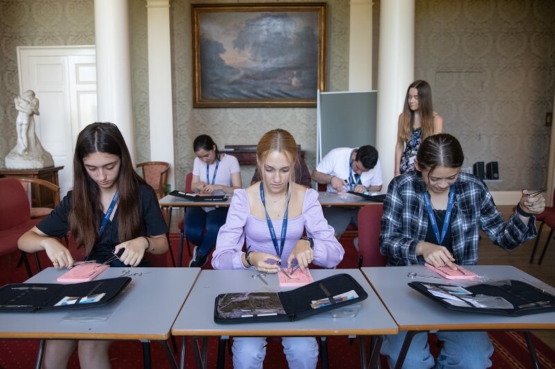 Students sat in rows in a classroom with individual sets of surgical tools to practice, preparing to practice. Students are taking part in an Immerse Education Medicine work experience