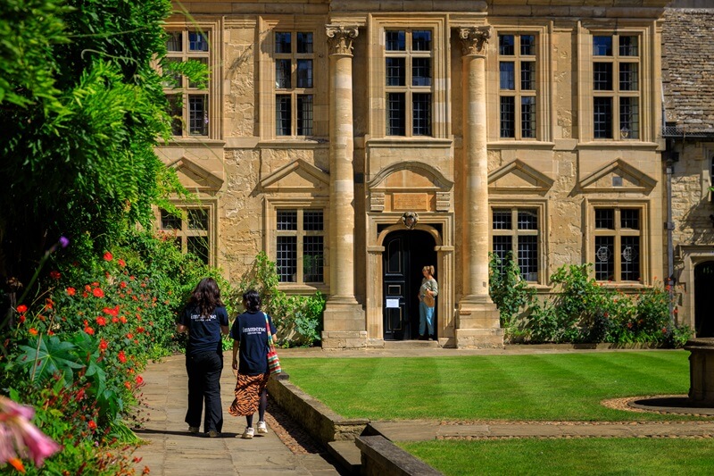 Immerse medicine students with their back to the camera, walking towards an Oxford University college on a sunny day during their summer school studies.